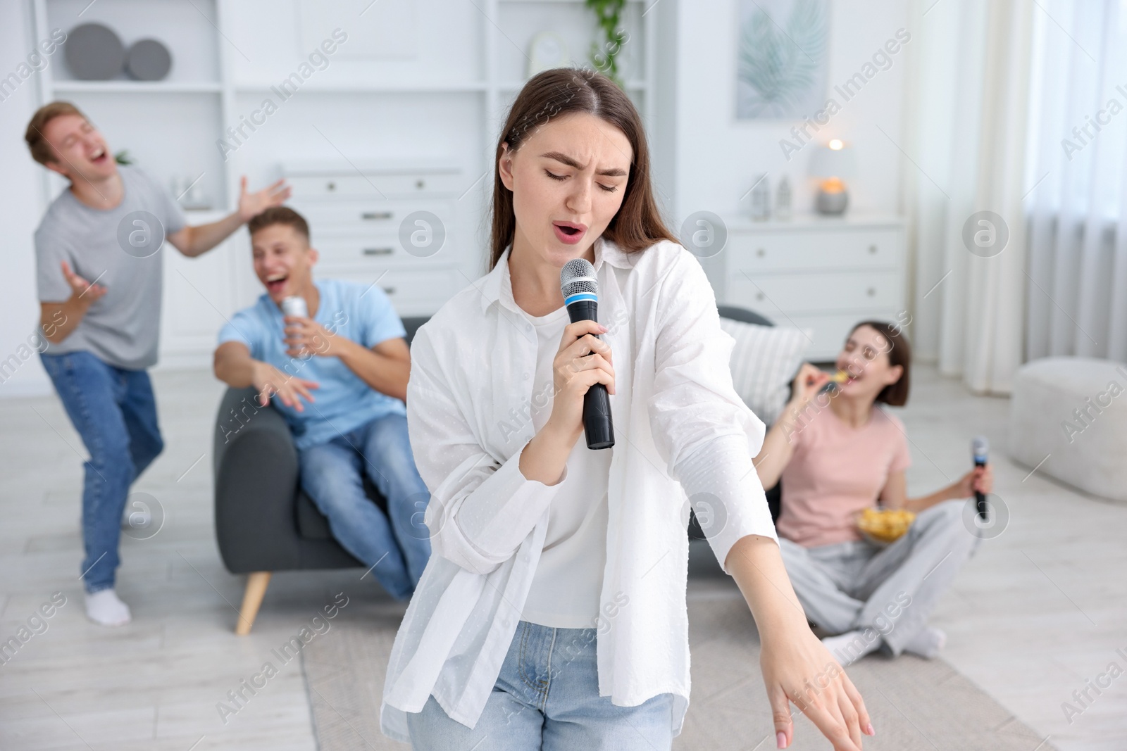 Photo of Young woman singing karaoke with friends at home, selective focus