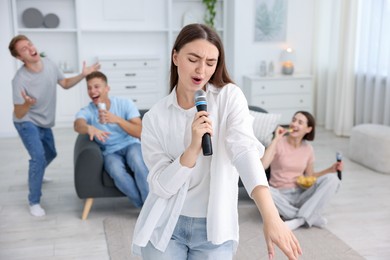 Photo of Young woman singing karaoke with friends at home, selective focus