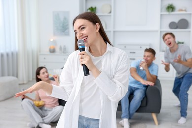 Photo of Young woman singing karaoke with friends at home, selective focus