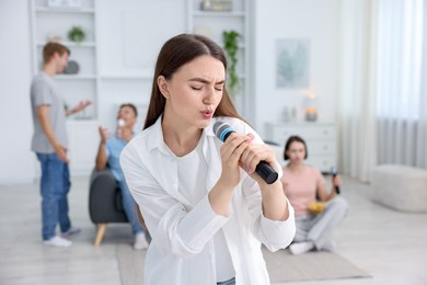 Photo of Young woman singing karaoke with friends at home, selective focus