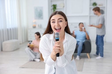 Photo of Young woman singing karaoke with friends at home, selective focus
