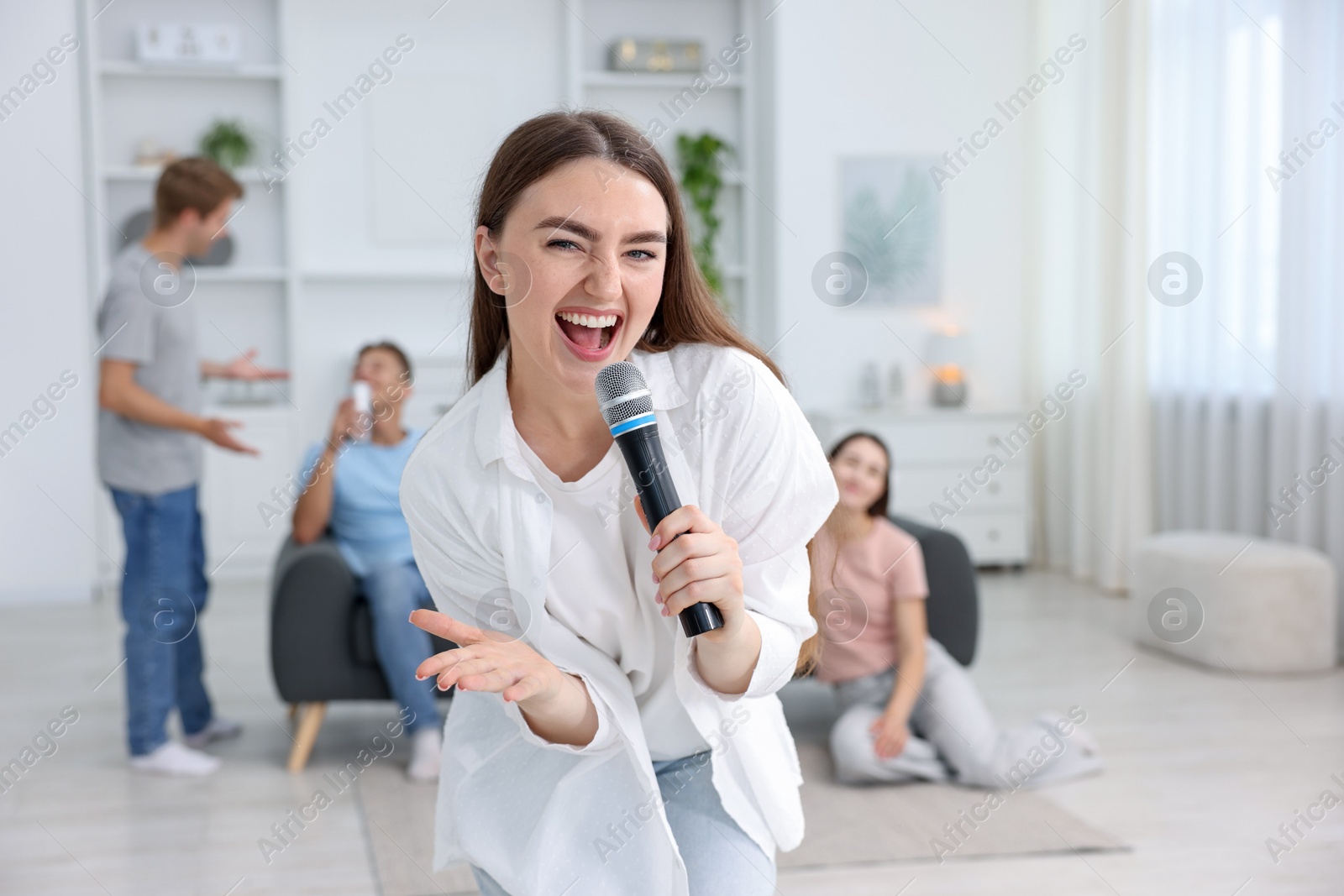 Photo of Young woman singing karaoke with friends at home, selective focus