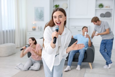 Photo of Young woman singing karaoke with friends at home, selective focus