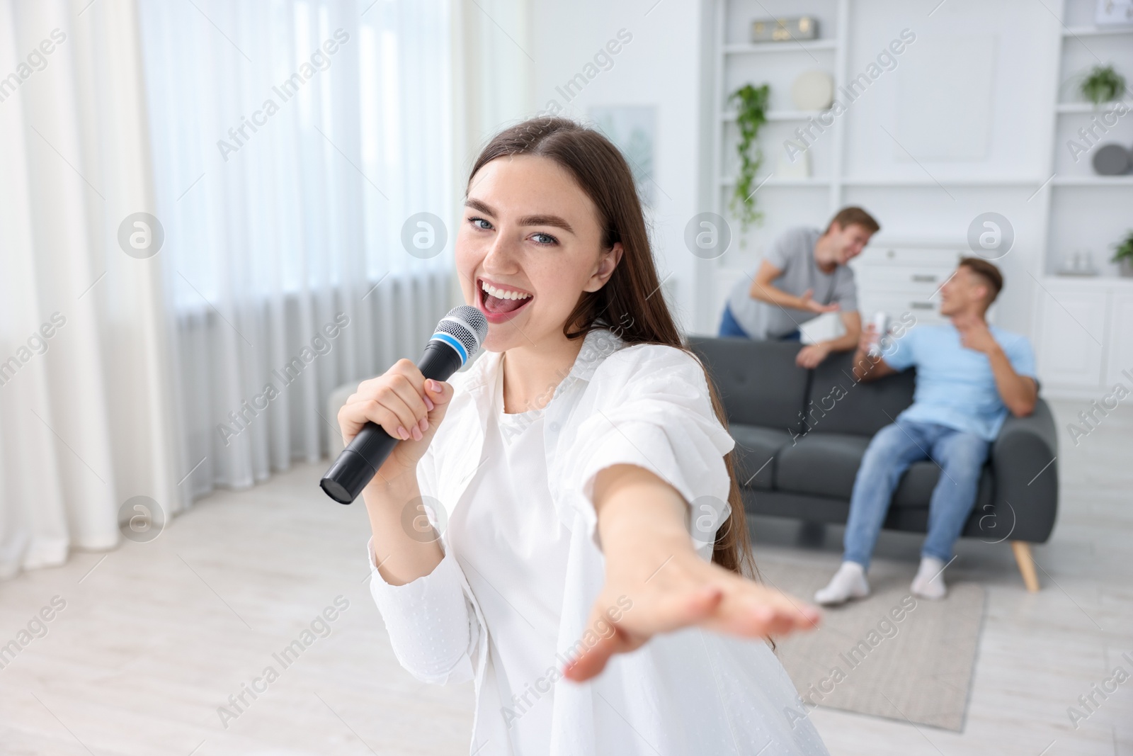 Photo of Young woman singing karaoke with friends at home, selective focus