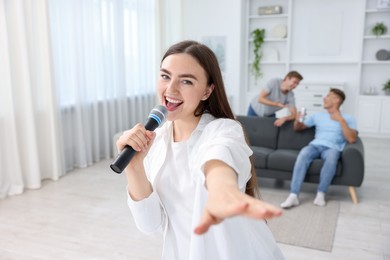 Photo of Young woman singing karaoke with friends at home, selective focus