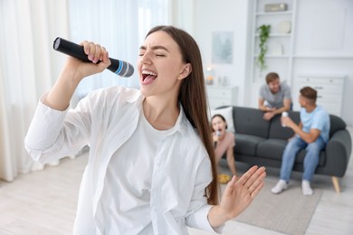 Photo of Young woman singing karaoke with friends at home, selective focus