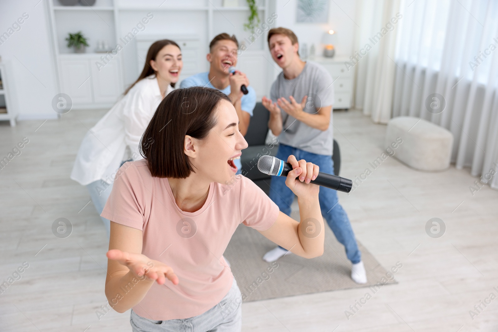 Photo of Young woman singing karaoke with friends at home, selective focus