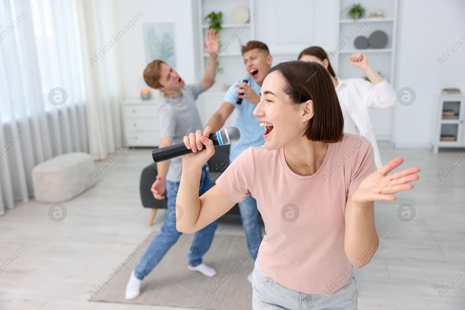 Photo of Young woman singing karaoke with friends at home, selective focus