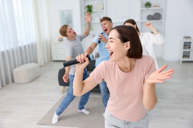 Photo of Young woman singing karaoke with friends at home, selective focus