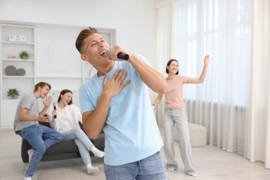 Photo of Young woman singing karaoke with friends at home, selective focus