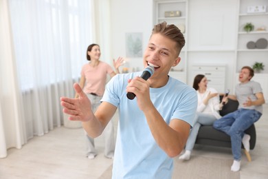 Photo of Young woman singing karaoke with friends at home, selective focus
