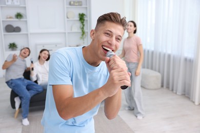 Photo of Young woman singing karaoke with friends at home, selective focus