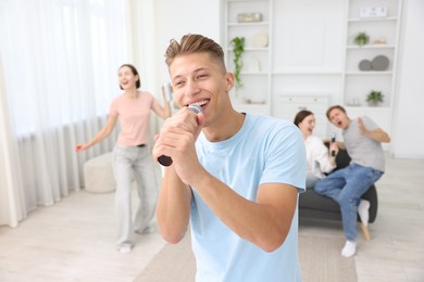 Photo of Young woman singing karaoke with friends at home, selective focus
