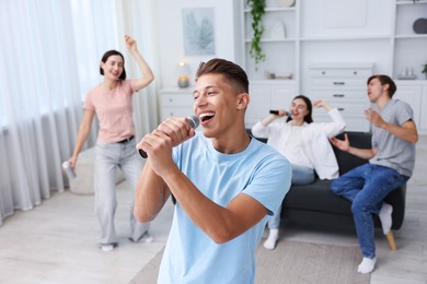Photo of Young woman singing karaoke with friends at home, selective focus