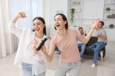 Photo of Young woman singing karaoke with friends at home, selective focus