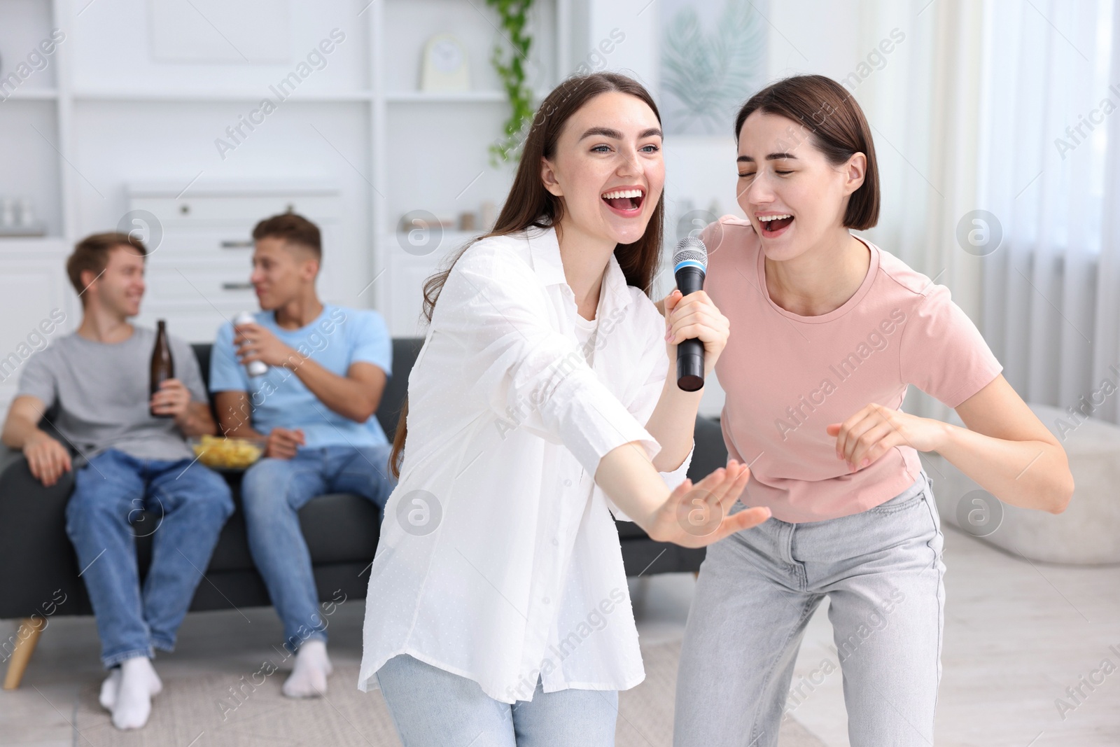 Photo of Young woman singing karaoke with friends at home, selective focus