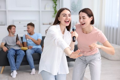 Photo of Young woman singing karaoke with friends at home, selective focus