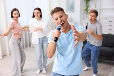 Photo of Young man singing karaoke with friends at home, selective focus