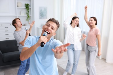 Photo of Young man singing karaoke with friends at home, selective focus