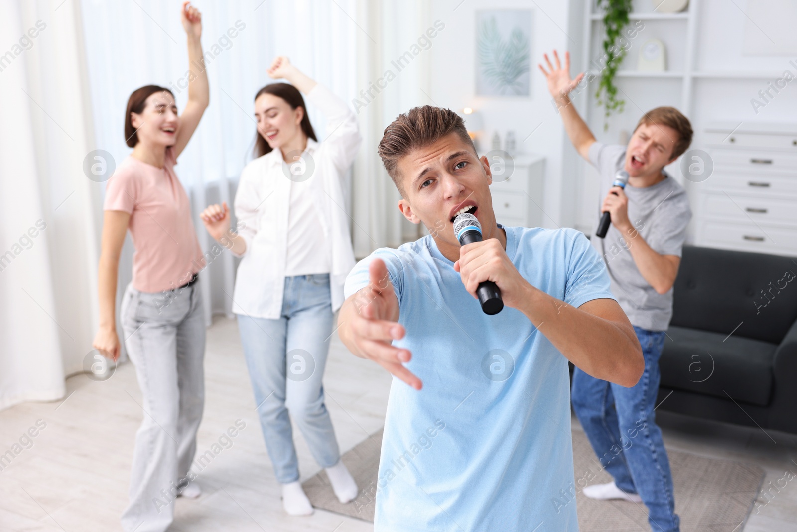 Photo of Young man singing karaoke with friends at home, selective focus