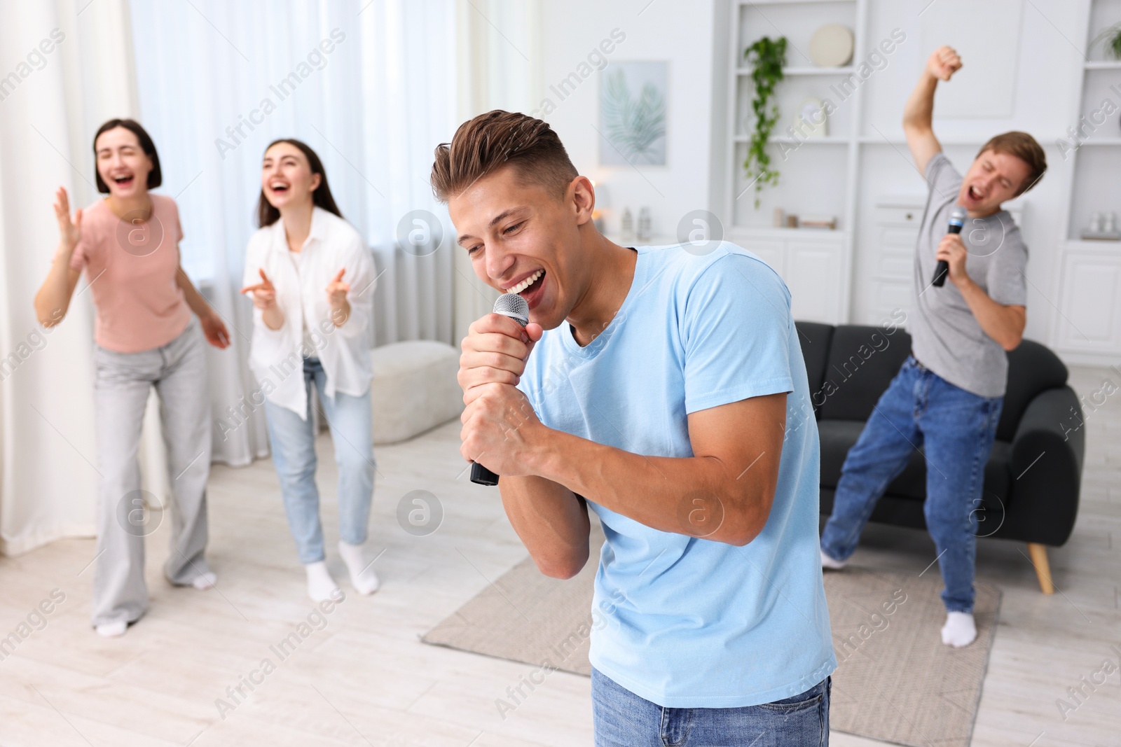 Photo of Young man singing karaoke with friends at home, selective focus