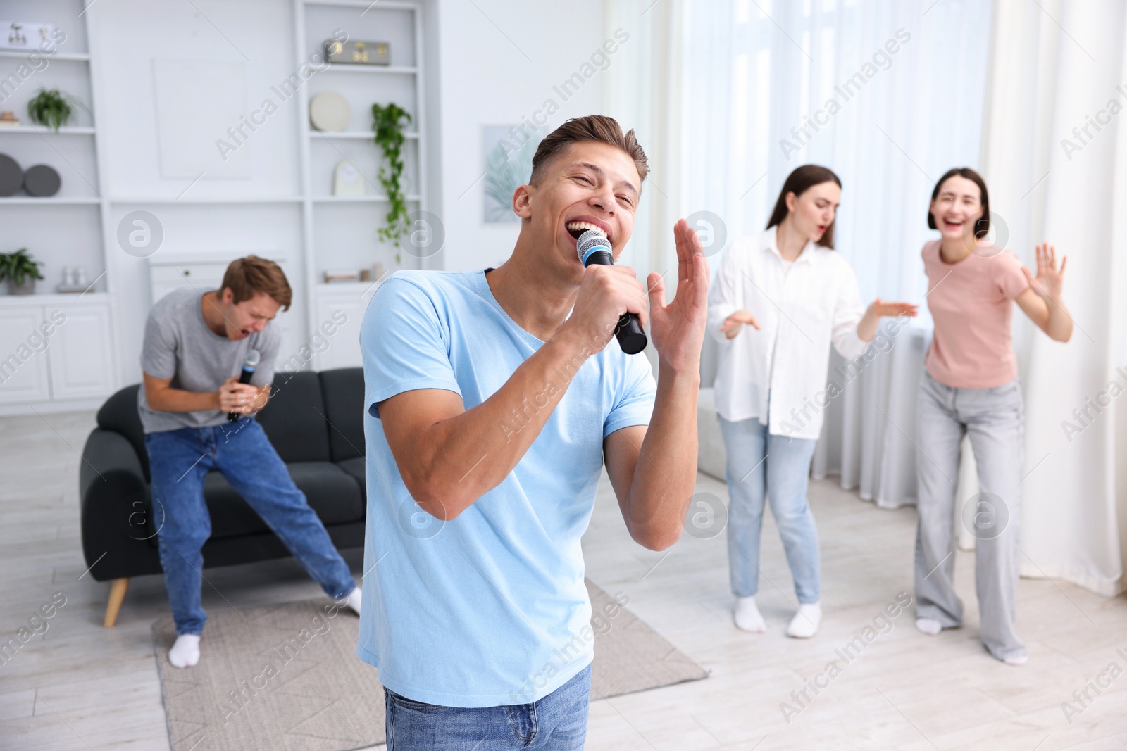 Photo of Young man singing karaoke with friends at home, selective focus