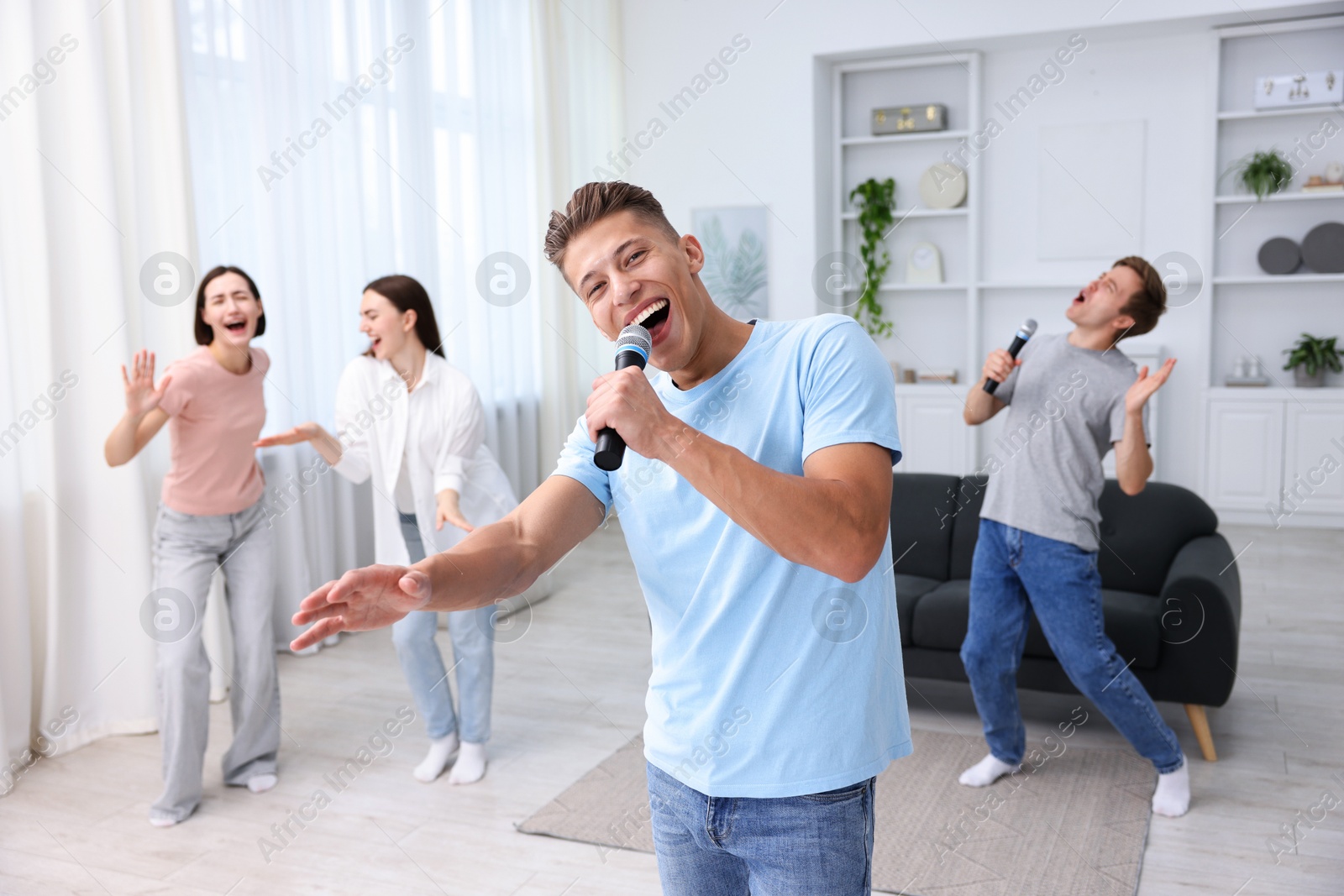 Photo of Young man singing karaoke with friends at home, selective focus