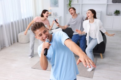 Photo of Young man singing karaoke with friends at home, selective focus