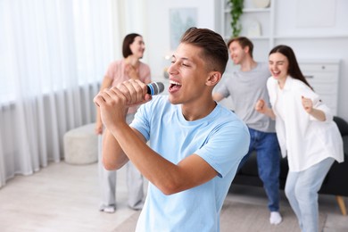Photo of Young man singing karaoke with friends at home, selective focus