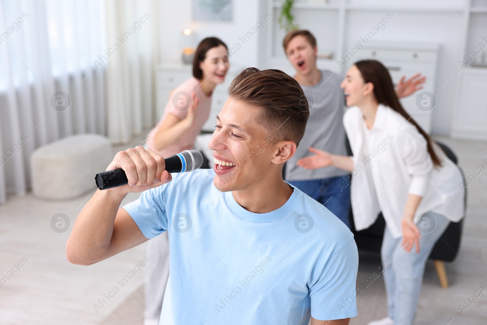 Photo of Young man singing karaoke with friends at home, selective focus