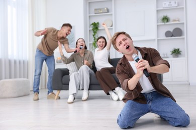 Photo of Young man singing karaoke with friends at home, selective focus