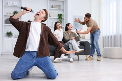Photo of Young man singing karaoke with friends at home, selective focus