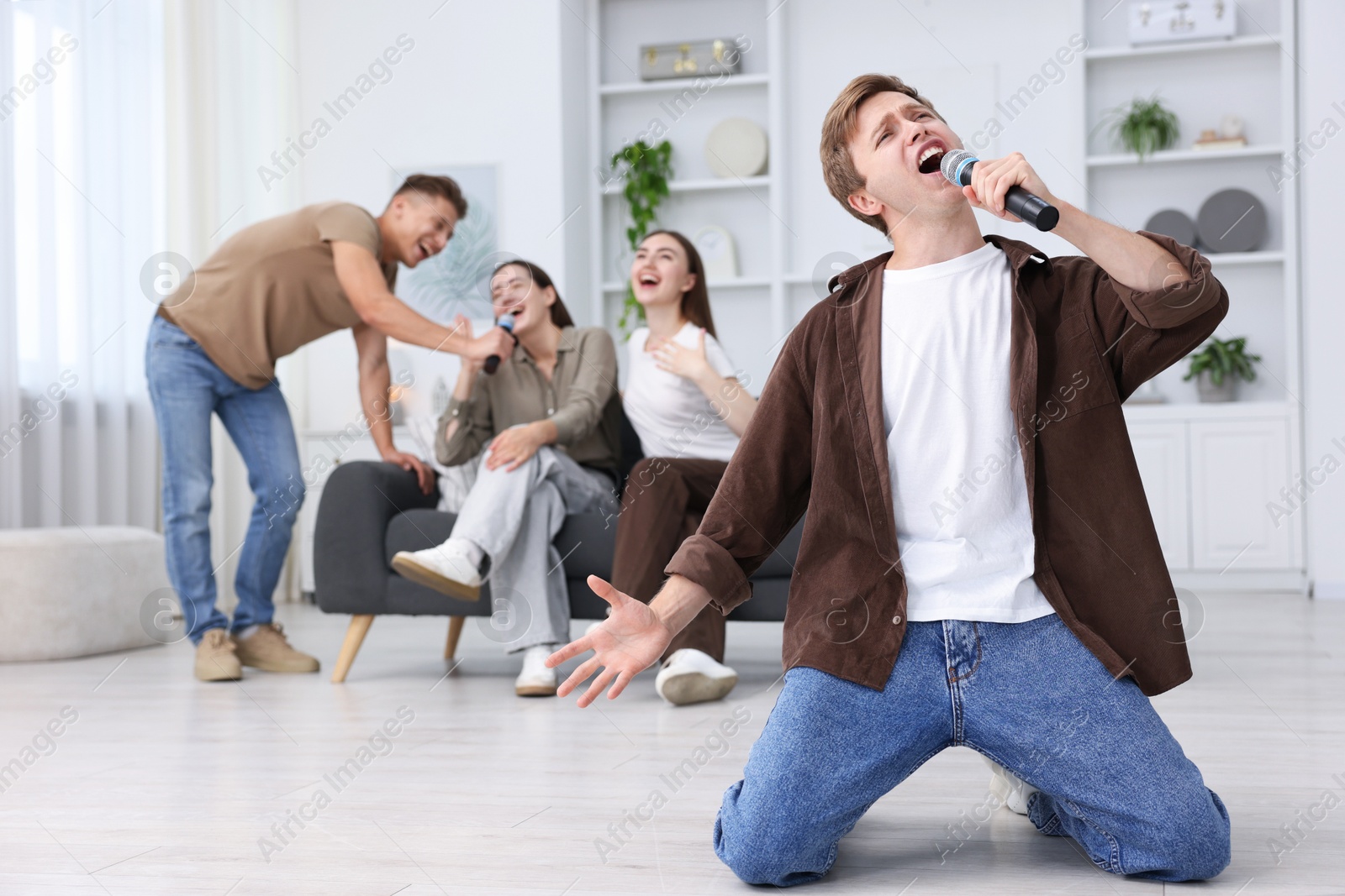 Photo of Young man singing karaoke with friends at home, selective focus