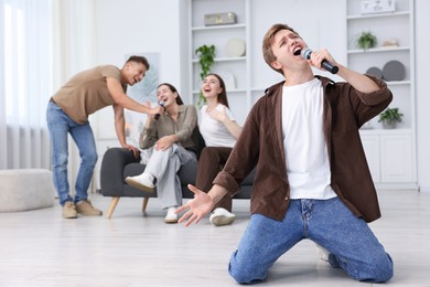 Photo of Young man singing karaoke with friends at home, selective focus