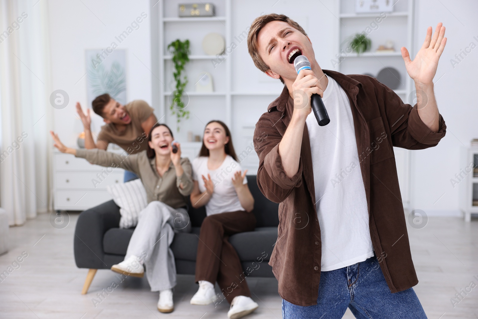 Photo of Young man singing karaoke with friends at home, selective focus