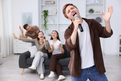 Photo of Young man singing karaoke with friends at home, selective focus