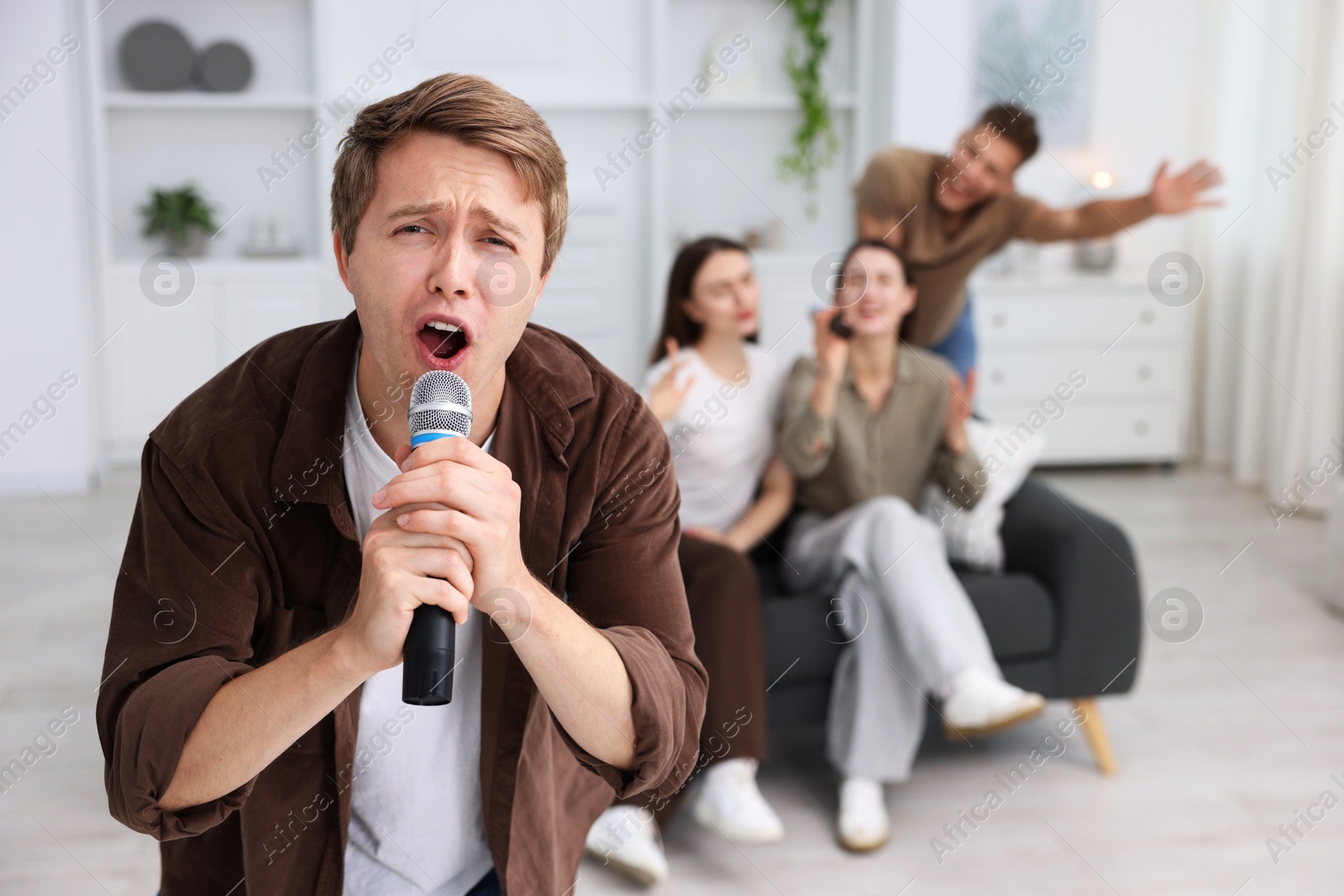 Photo of Young man singing karaoke with friends at home, selective focus