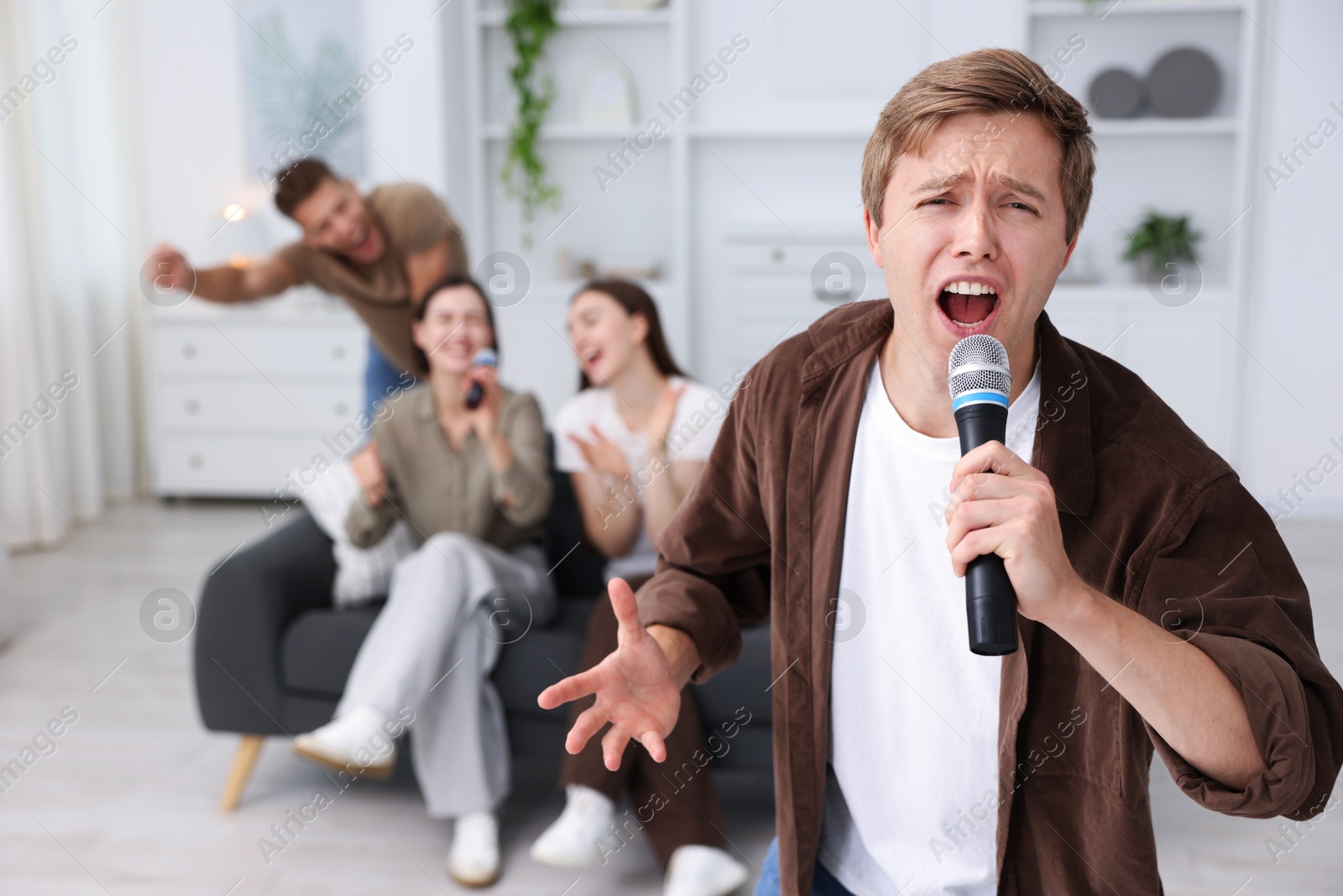 Photo of Young man singing karaoke with friends at home, selective focus