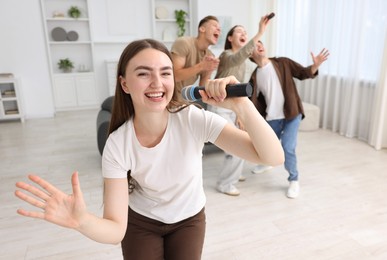Photo of Young woman singing karaoke with friends at home, selective focus