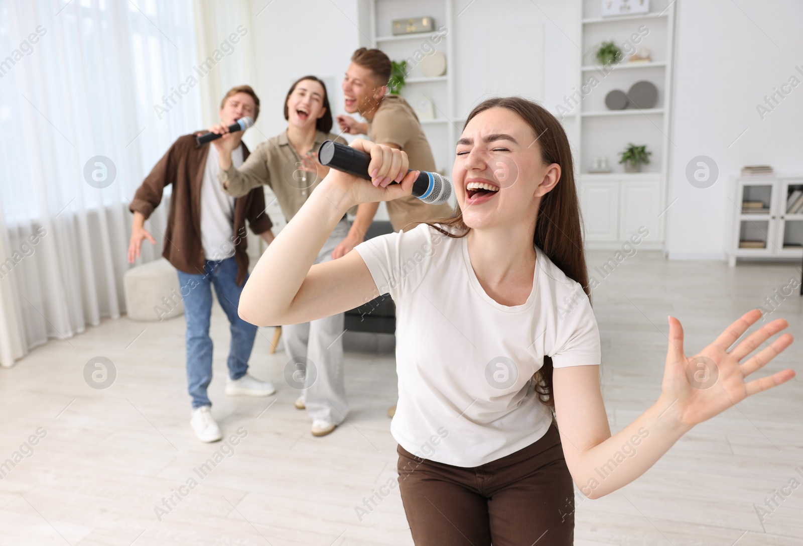 Photo of Young woman singing karaoke with friends at home, selective focus