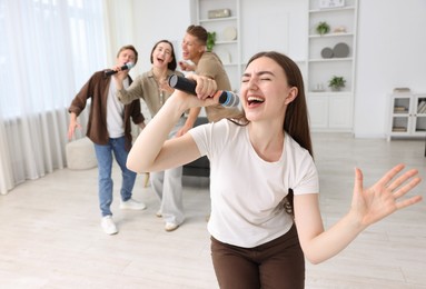 Photo of Young woman singing karaoke with friends at home, selective focus