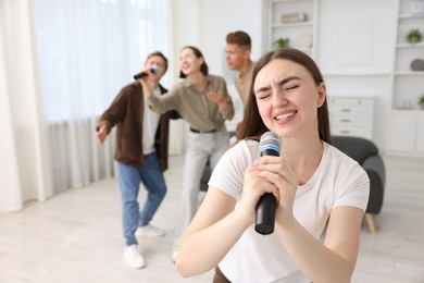 Photo of Young woman singing karaoke with friends at home, selective focus