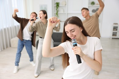 Photo of Young woman singing karaoke with friends at home, selective focus