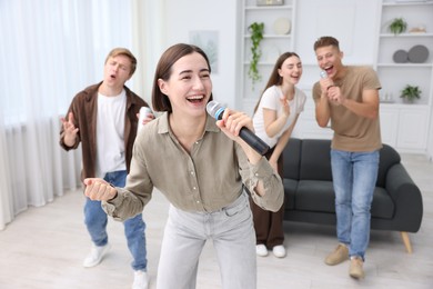 Photo of Young woman singing karaoke with friends at home, selective focus