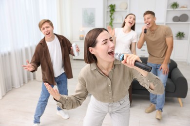 Photo of Young woman singing karaoke with friends at home, selective focus