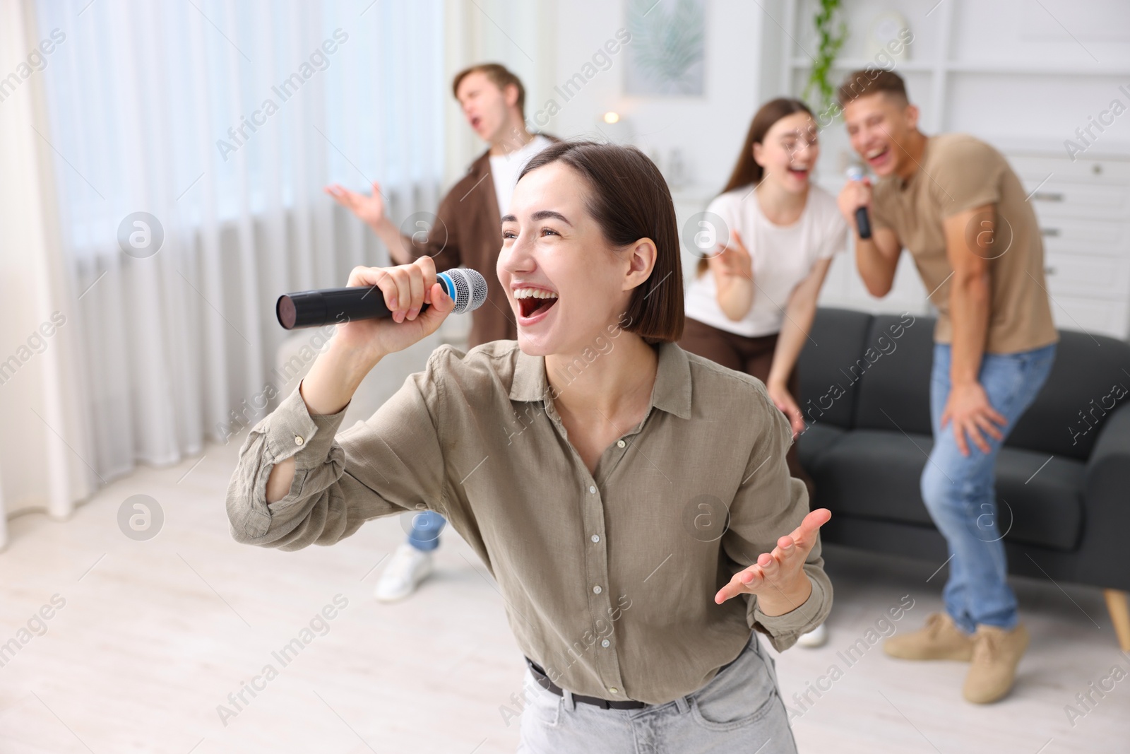 Photo of Young woman singing karaoke with friends at home, selective focus