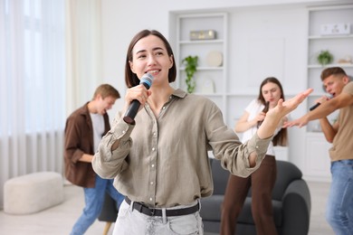 Photo of Young woman singing karaoke with friends at home, selective focus