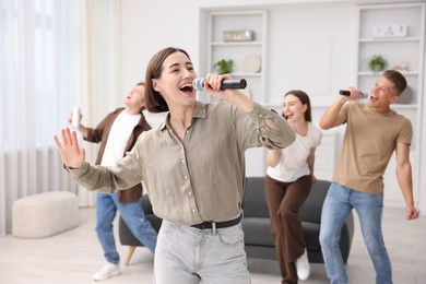 Photo of Young woman singing karaoke with friends at home, selective focus