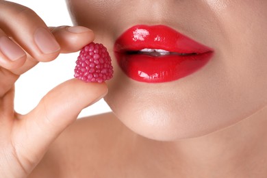 Photo of Woman with beautiful red lipstick on her lips and raspberry candy against white background, closeup
