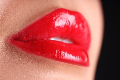 Photo of Woman with beautiful red lipstick on her lips against black background, macro view